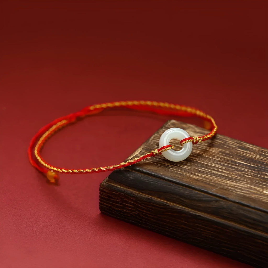 Red rope braided bracelet with natural wave-shaped Hetian jade pendant for Tiger Year birth year, on a neutral background