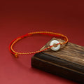 Red rope braided bracelet with natural wave-shaped Hetian jade pendant for Tiger Year birth year, on a neutral background
