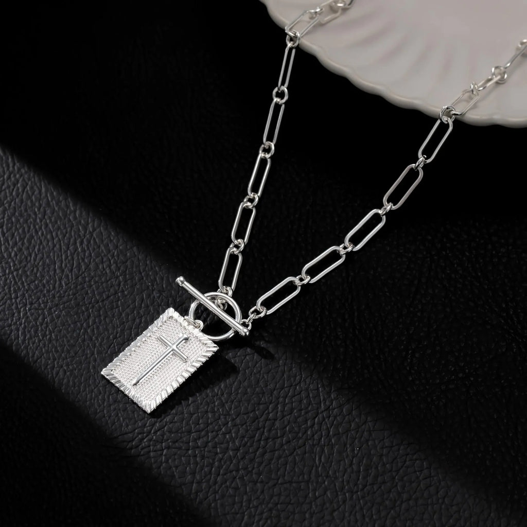 Gold electroplated stainless steel clip chain necklace with cross and square geometric pendant on white background