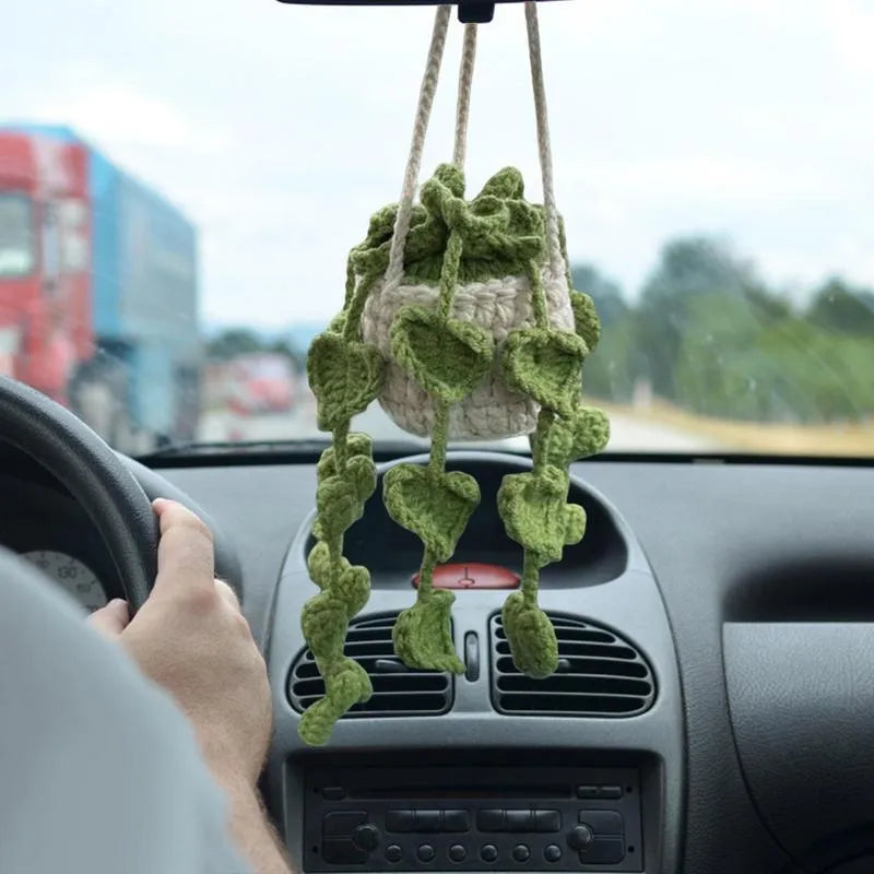 Green and white knitted wool car plant decoration with hanging rope on a car dashboard.