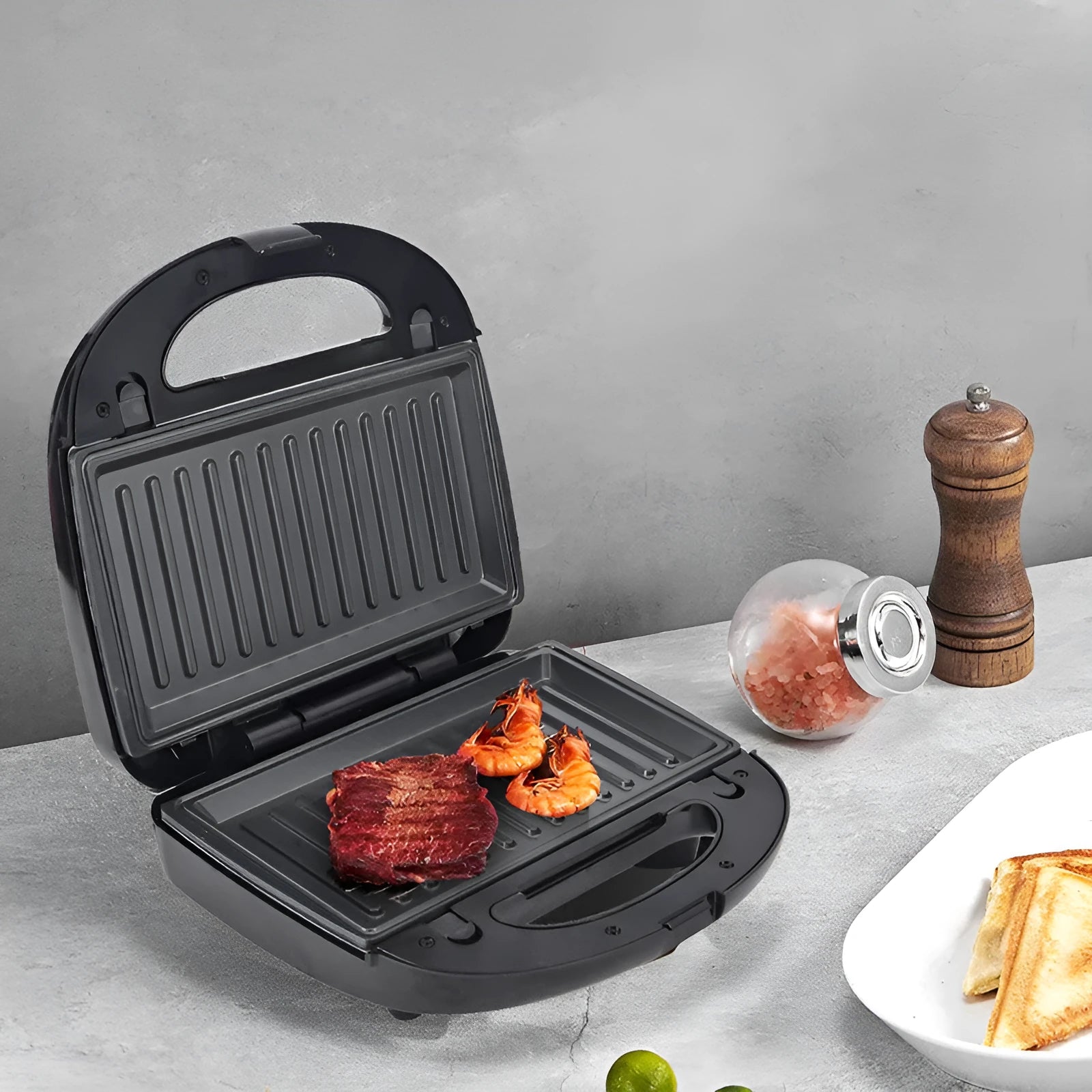Black double-sided electric sandwich pan with stainless steel lid on a kitchen counter.