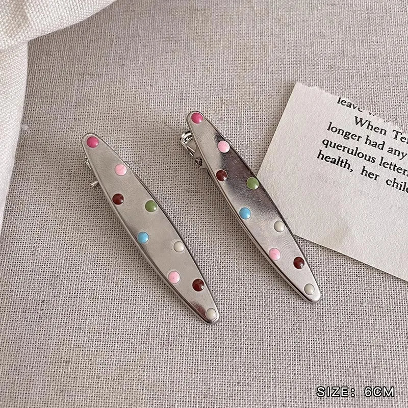 Two shiny silver metal duckbill barrettes with hollow star patterns on a plain background