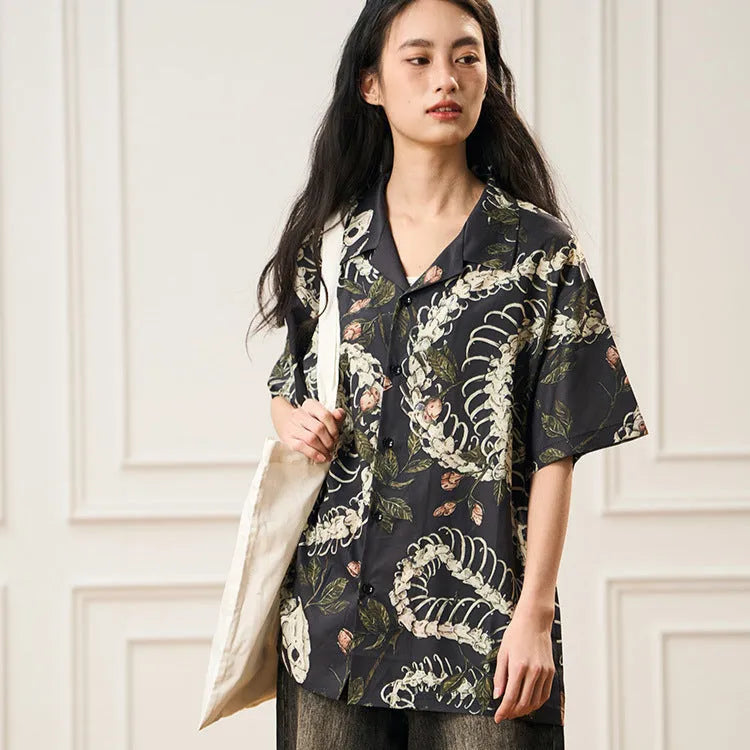 Man wearing a loose fit Cuban collar shirt with a printed snake bone and floral pattern in a summer setting.