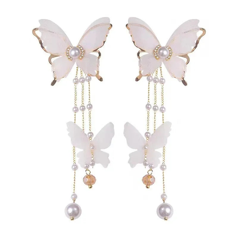A pair of white butterfly-shaped earrings with pearls, rhinestones, and a dangling lace tassel.
