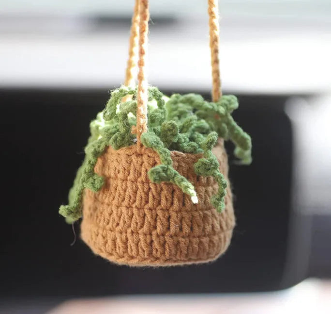 Green and white knitted wool car plant decoration with hanging rope on a car dashboard.