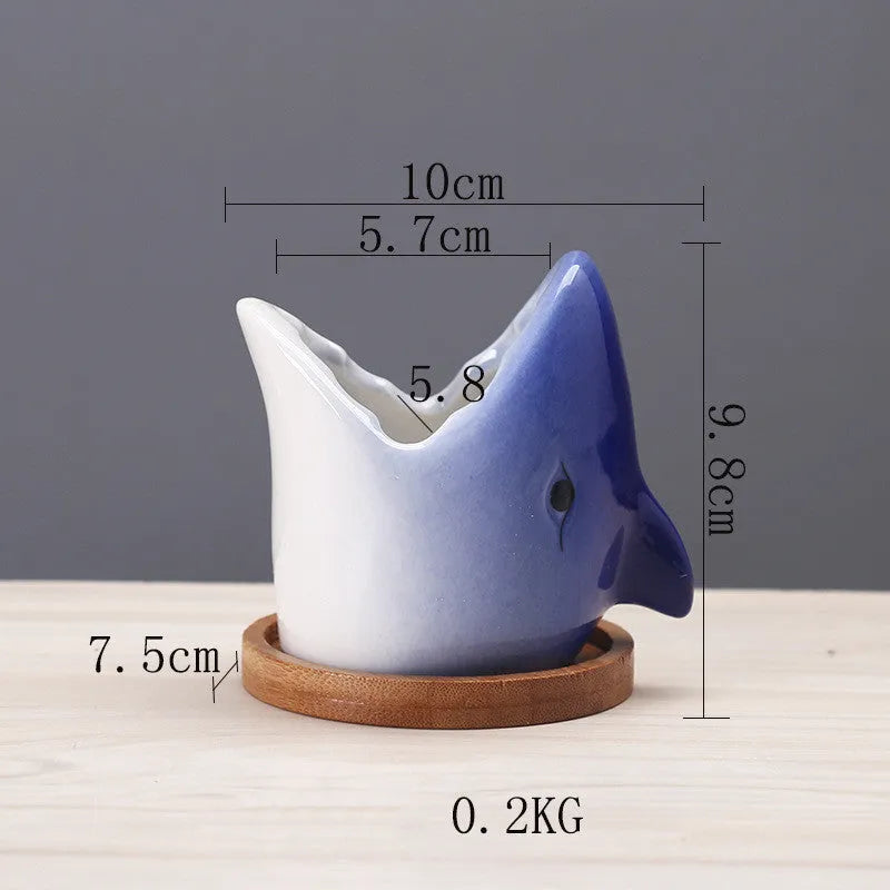 Creative cartoon ceramic succulent pot with drainage hole, blue colour, on a desk with a small succulent plant.
