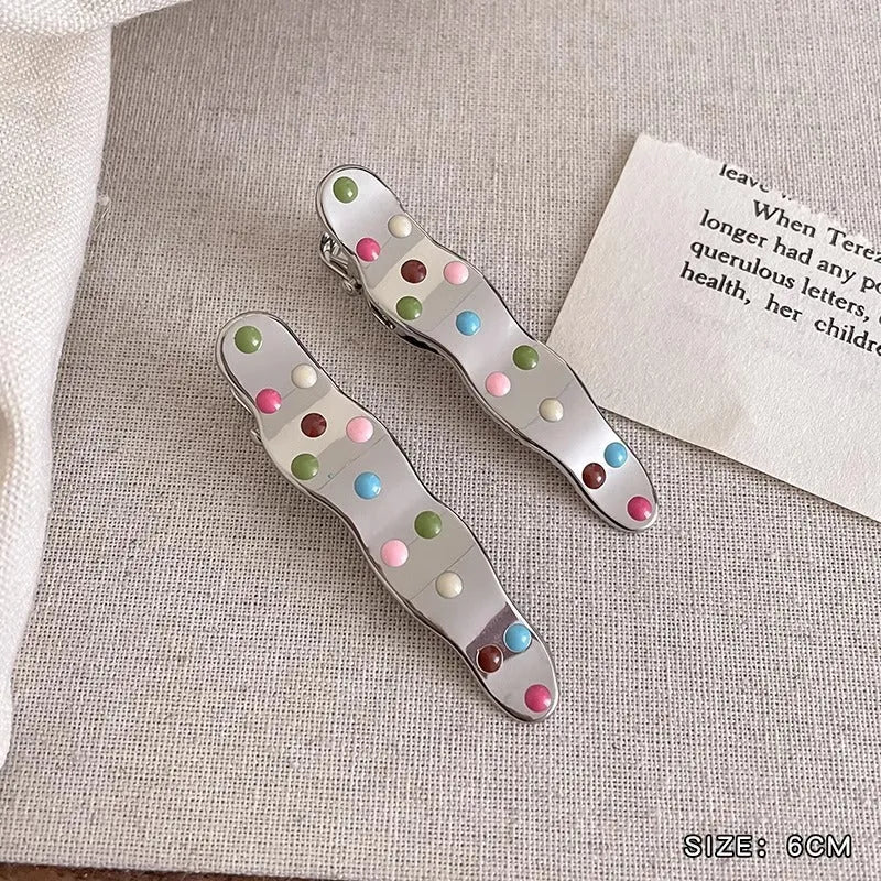 Two shiny silver metal duckbill barrettes with hollow star patterns on a plain background