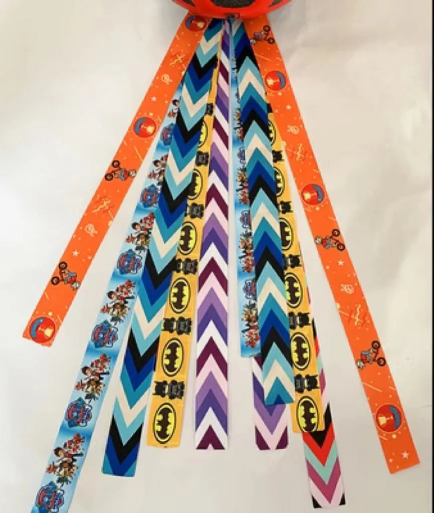 Colourful fabric helmet streamers for children's roller skating and ski helmets, shown in apricot, red, and grey.