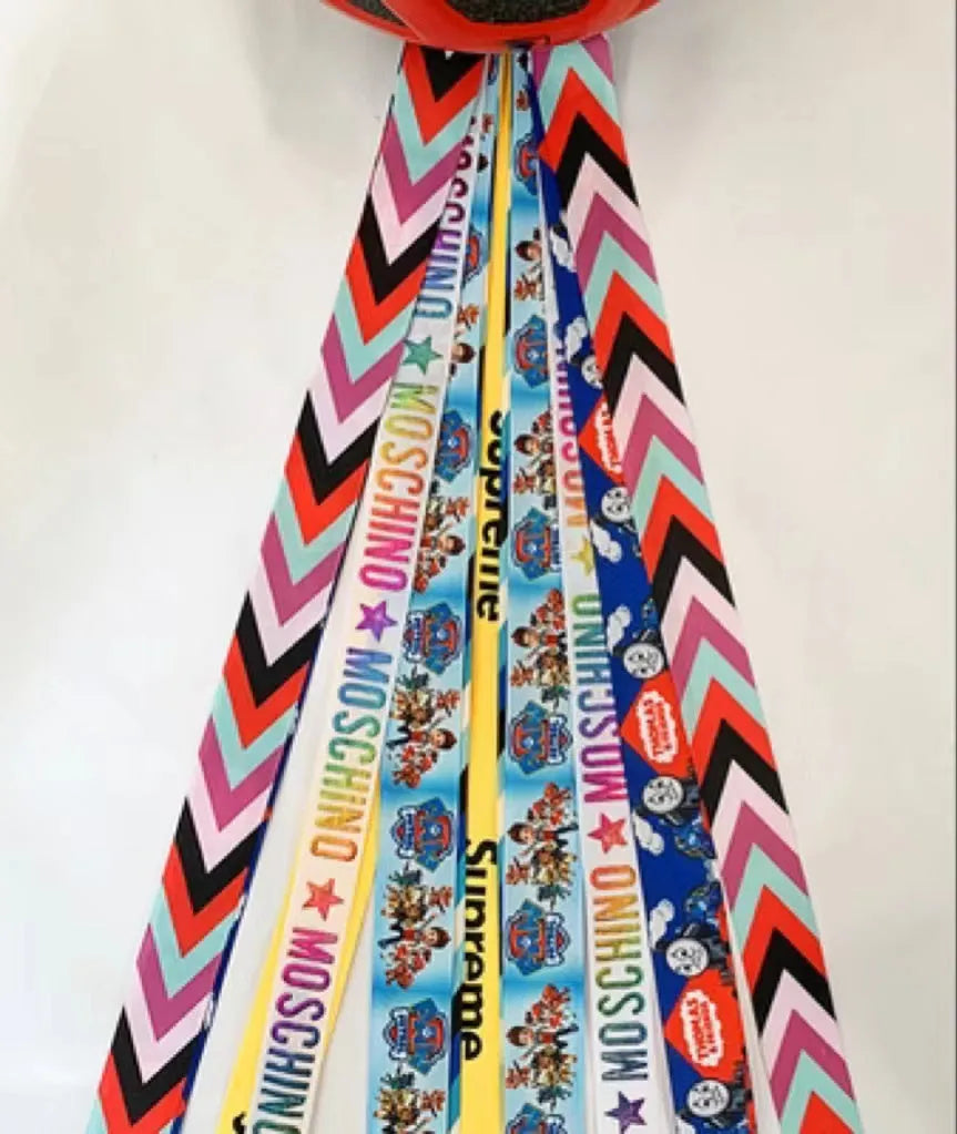 Colourful fabric helmet streamers for children's roller skating and ski helmets, shown in apricot, red, and grey.