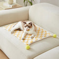 Green plaid pet fleece blanket with fur ball decoration on a sofa for a cat or dog.