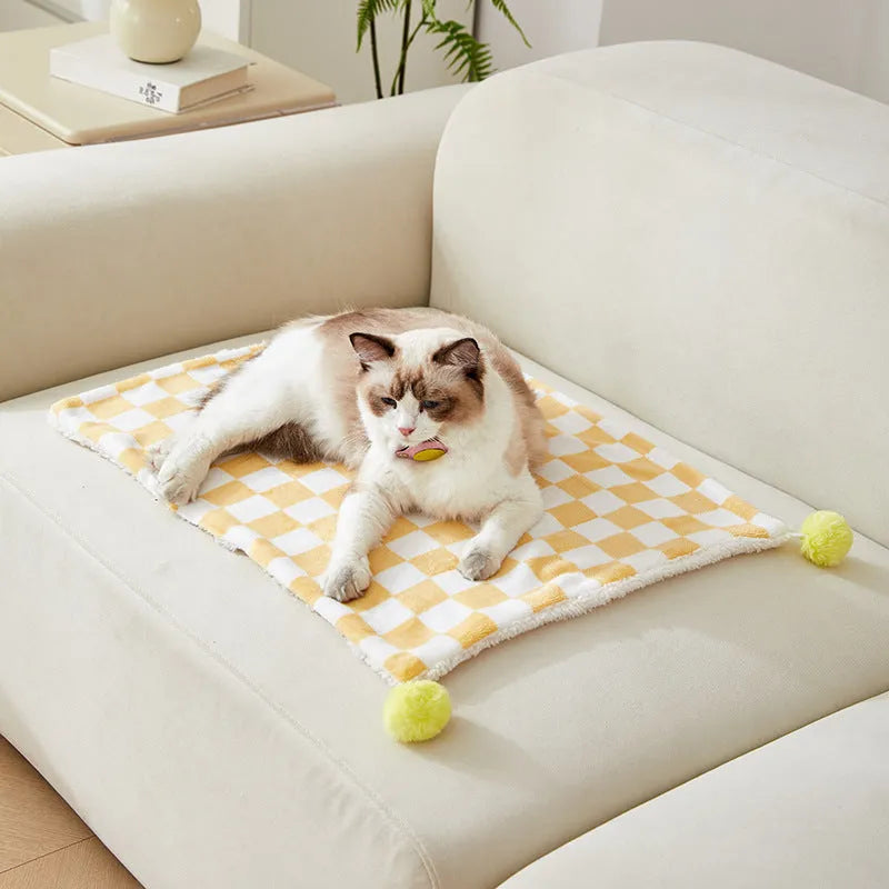 Green plaid pet fleece blanket with fur ball decoration on a sofa for a cat or dog.