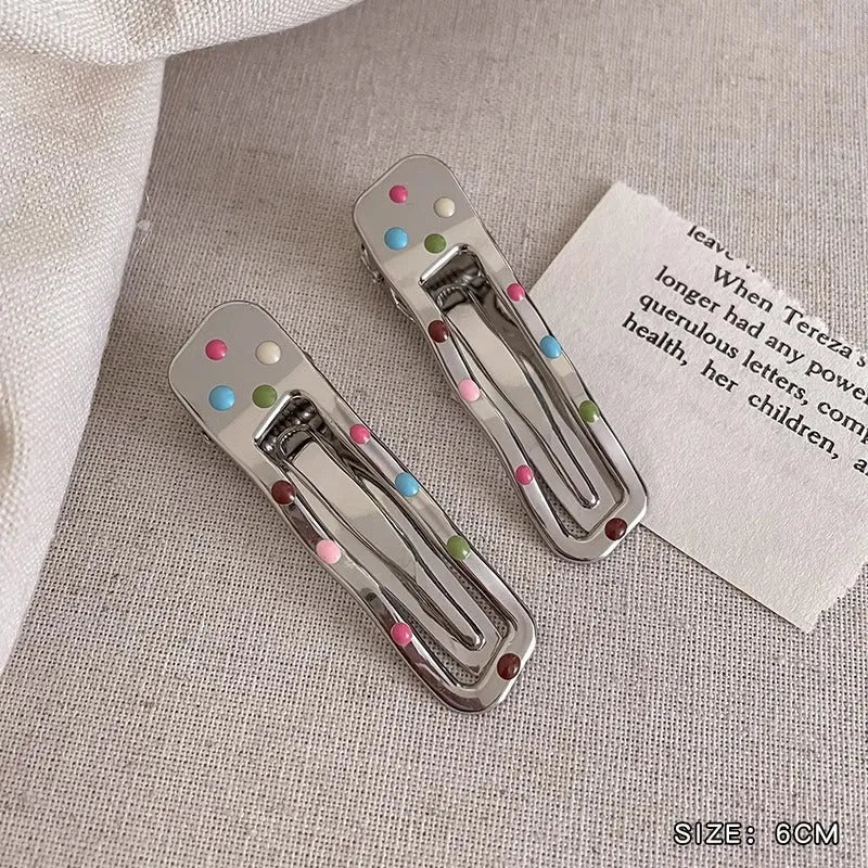 Two shiny silver metal duckbill barrettes with hollow star patterns on a plain background