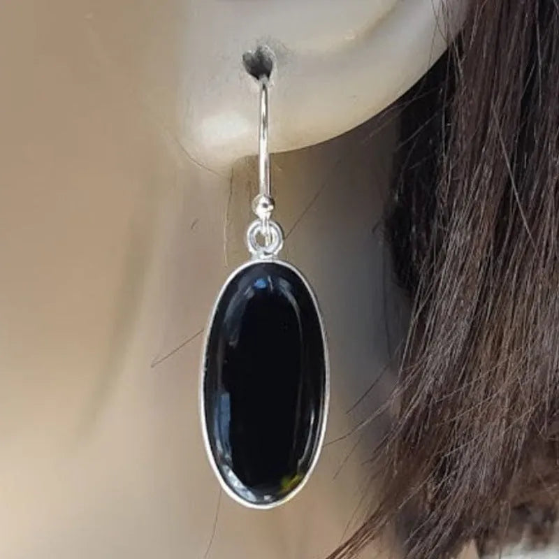 Oval black agate stone set in a geometric silver electroplated frame, forming a drop pendant earring for women.