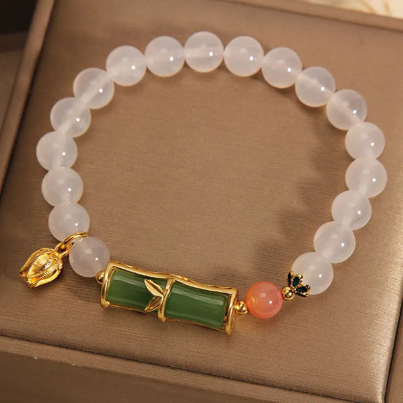 Close-up of a women's bracelet with a white agate jade bead and bamboo joint design on a natural background.