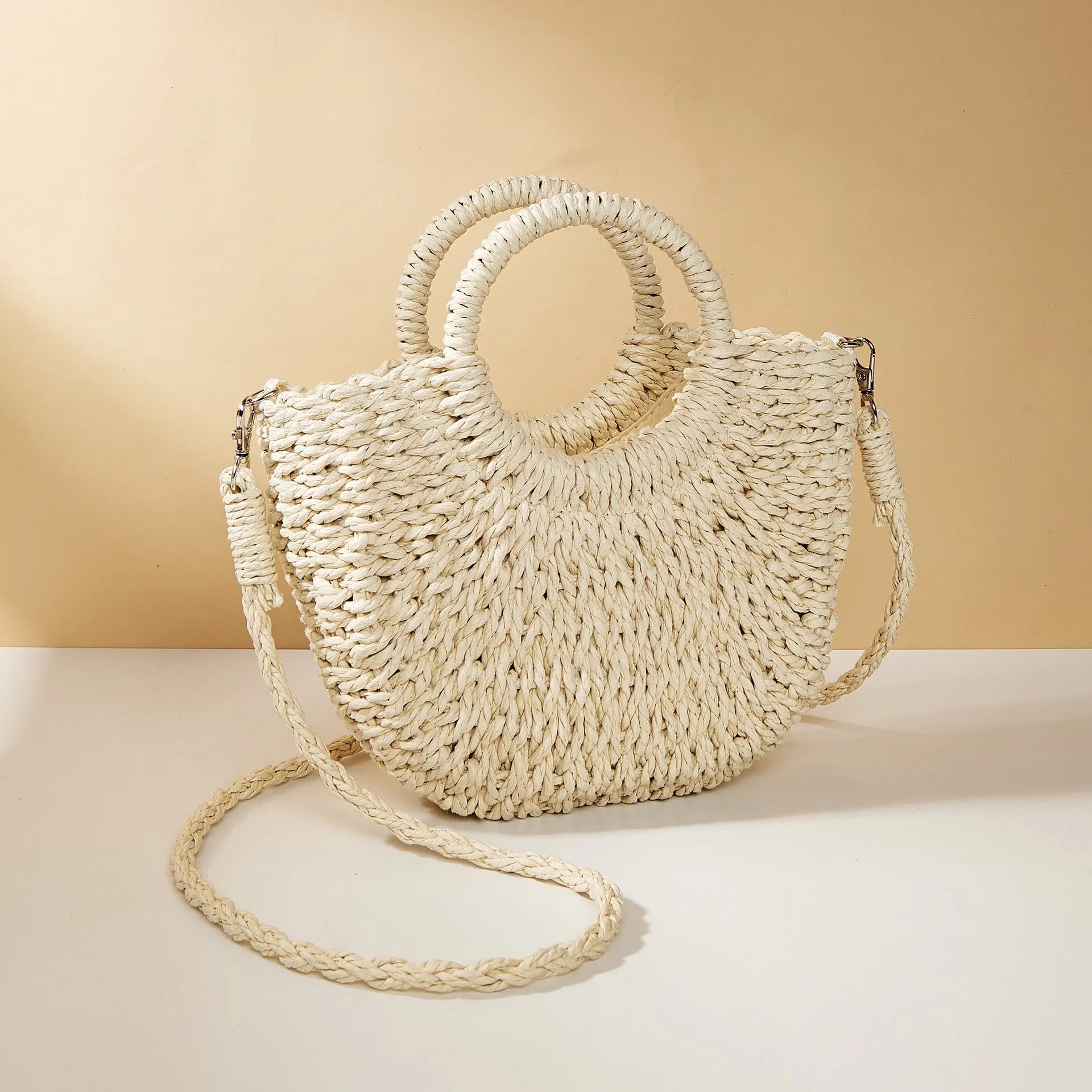 Woven straw beach bag in beige, peach skin lining, crossbody style, 24cm height, on a sandy beach