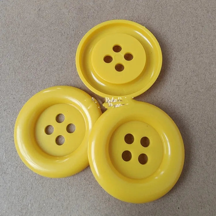 Assortment of oversized round plastic buttons in multiple colours with four stitching holes.