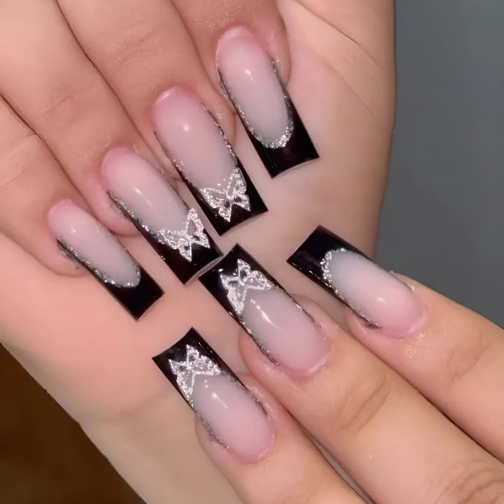 Black French-style false nails with glitter butterfly design on a hand.