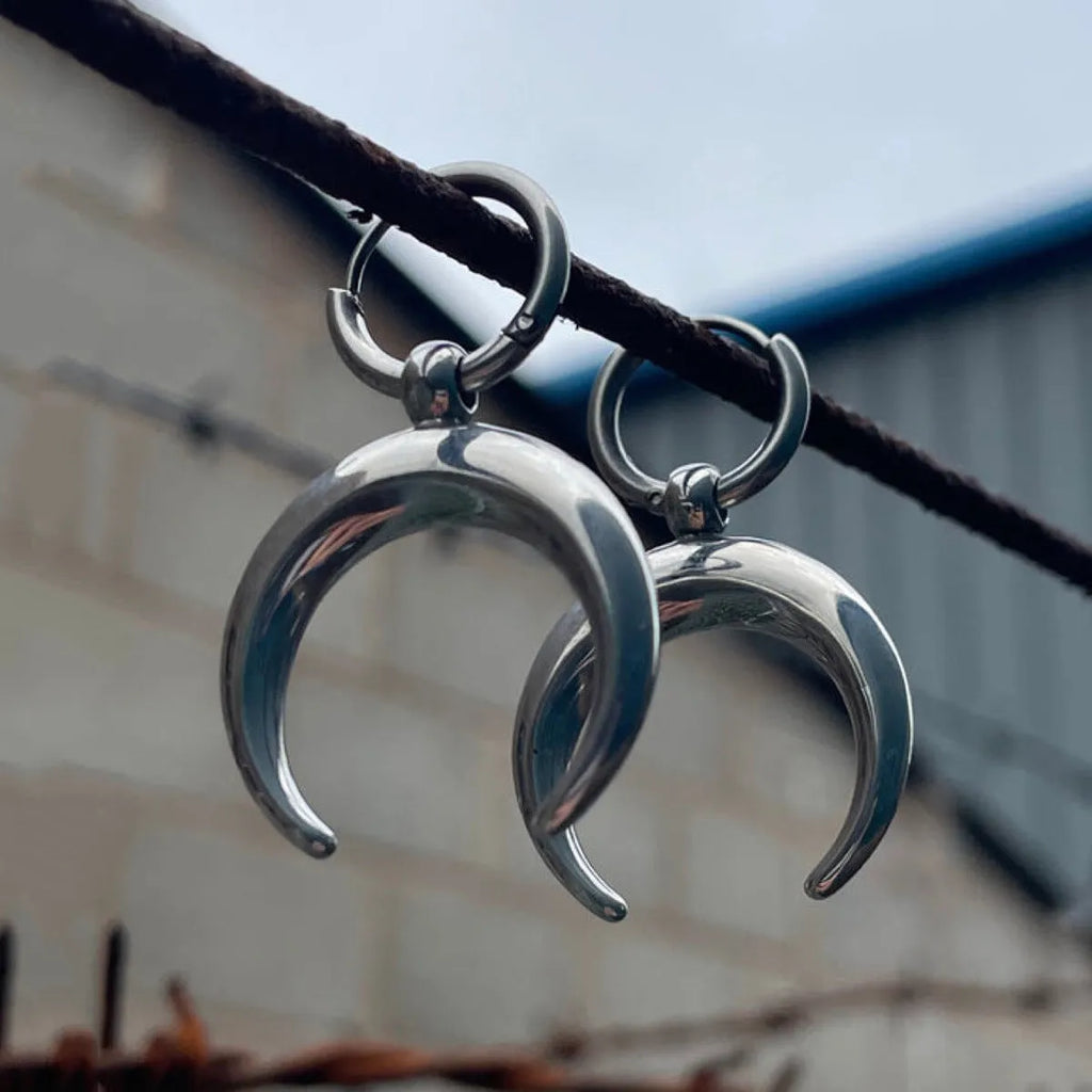 A pair of large silver geometric hoop earrings with a detailed Gothic moon motif, shown as clip-ons.