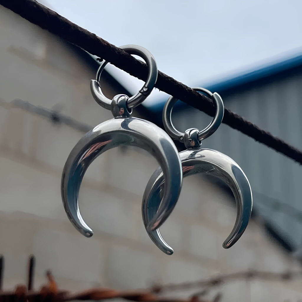 A pair of large silver geometric hoop earrings with a detailed Gothic moon motif, shown as clip-ons.