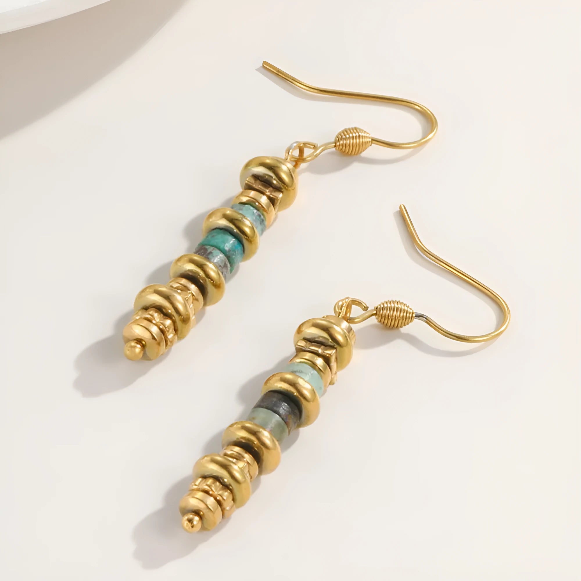 A pair of geometric-shaped, gold-coloured titanium steel dangle earrings on a white background.