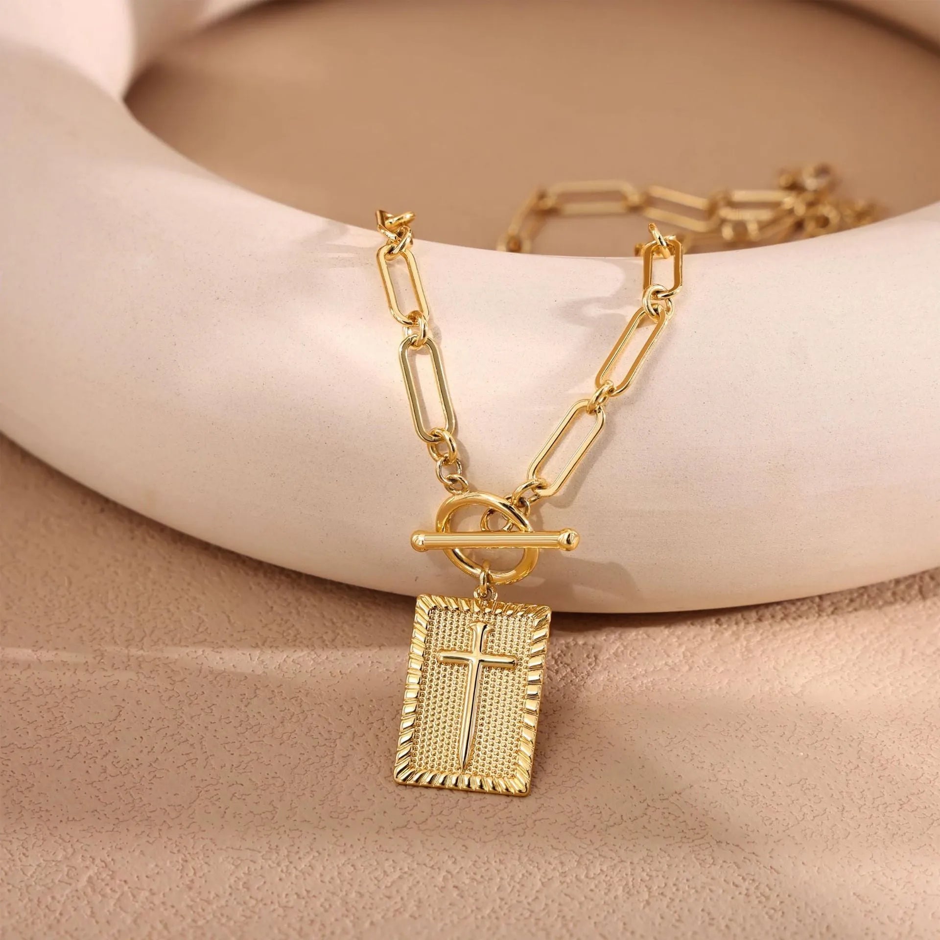 Gold electroplated stainless steel clip chain necklace with cross and square geometric pendant on white background