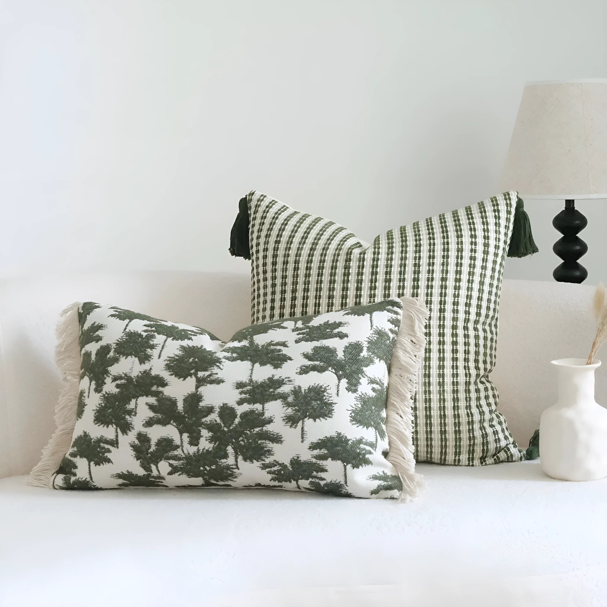 Green striped and botanical patterned hotel sample pillow with tassels on a bed display.