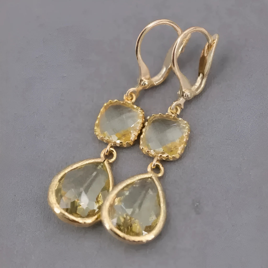 Gold geometric dangle earrings with a long fringe and water droplet design on a white background.