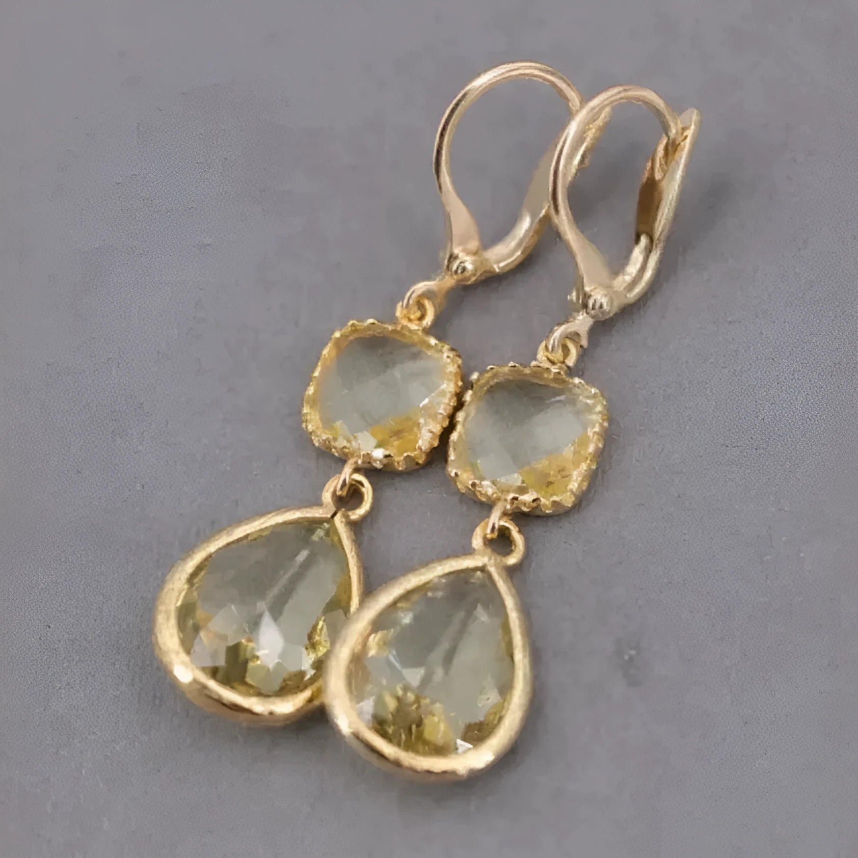 Gold geometric dangle earrings with a long fringe and water droplet design on a white background.