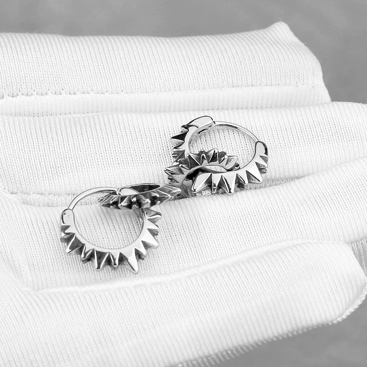 A pair of polished stainless steel round ring earrings in a steel colour finish on a plain background.