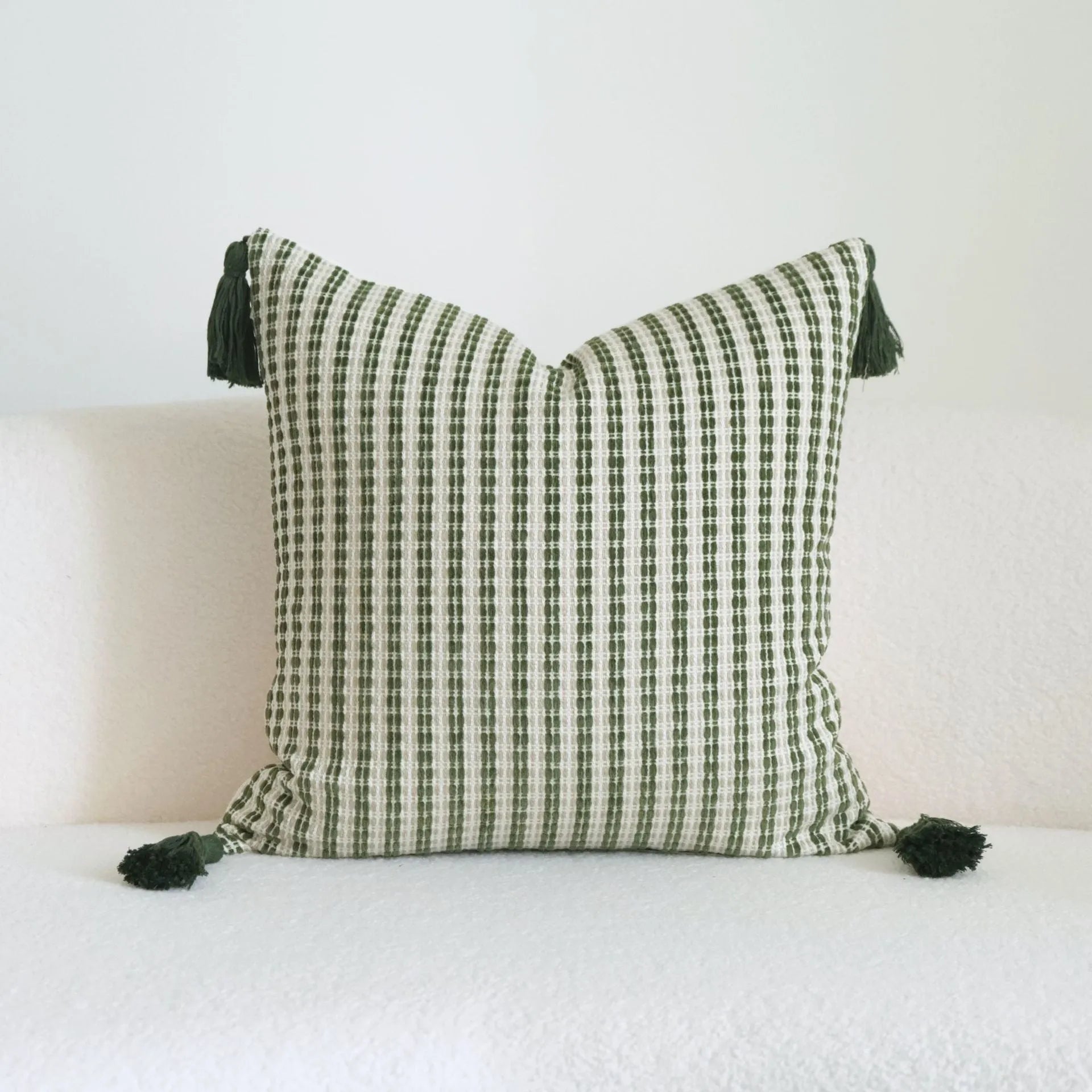 Green striped and botanical patterned hotel sample pillow with tassels on a bed display.