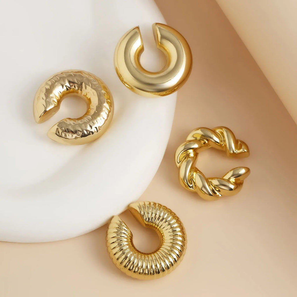 Set of four geometric gold and silver clip-on earrings for women on a flat surface.