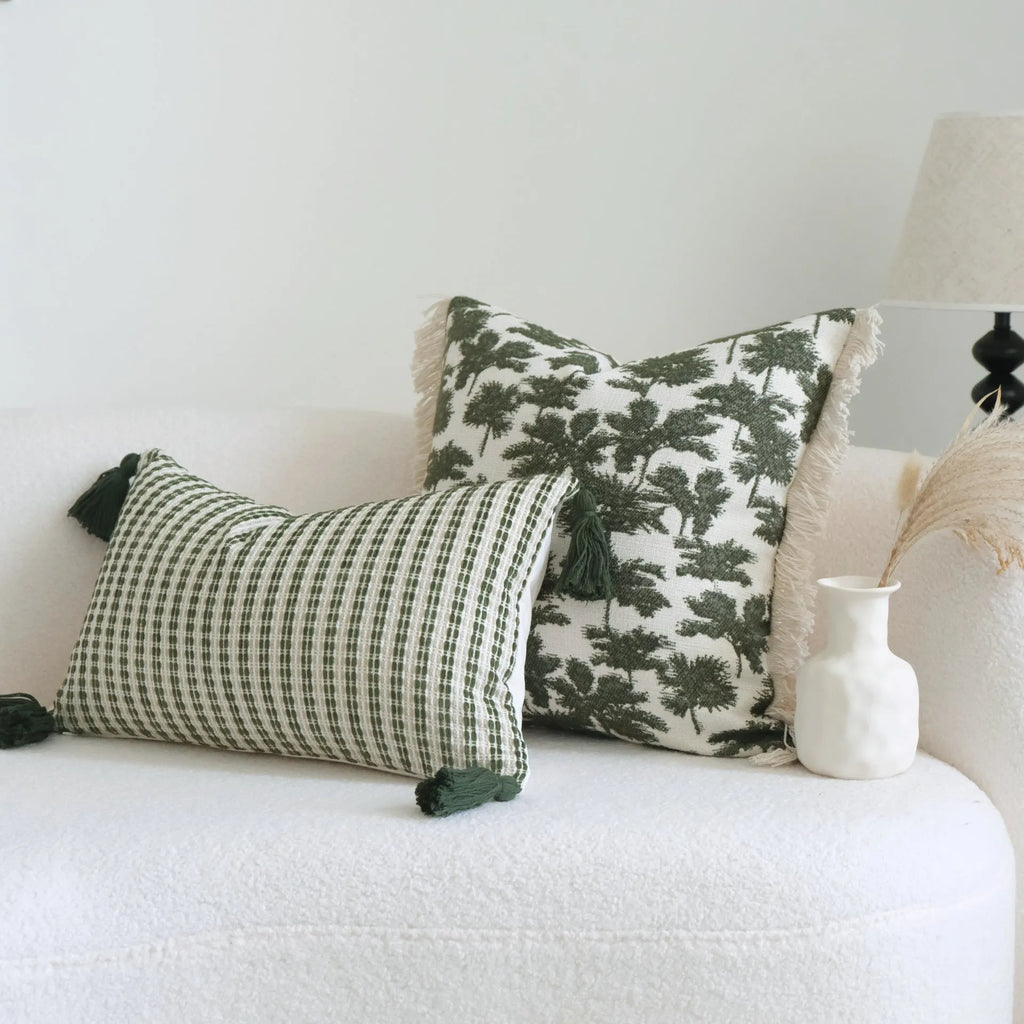 Green striped and botanical patterned hotel sample pillow with tassels on a bed display.