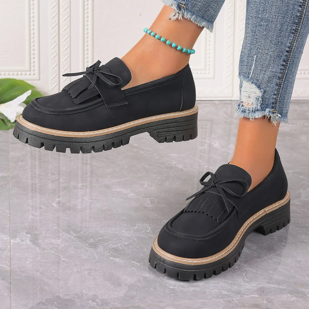 Women's black plus size loafers with a tassel and bowknot decoration and a chunky rubber sole.