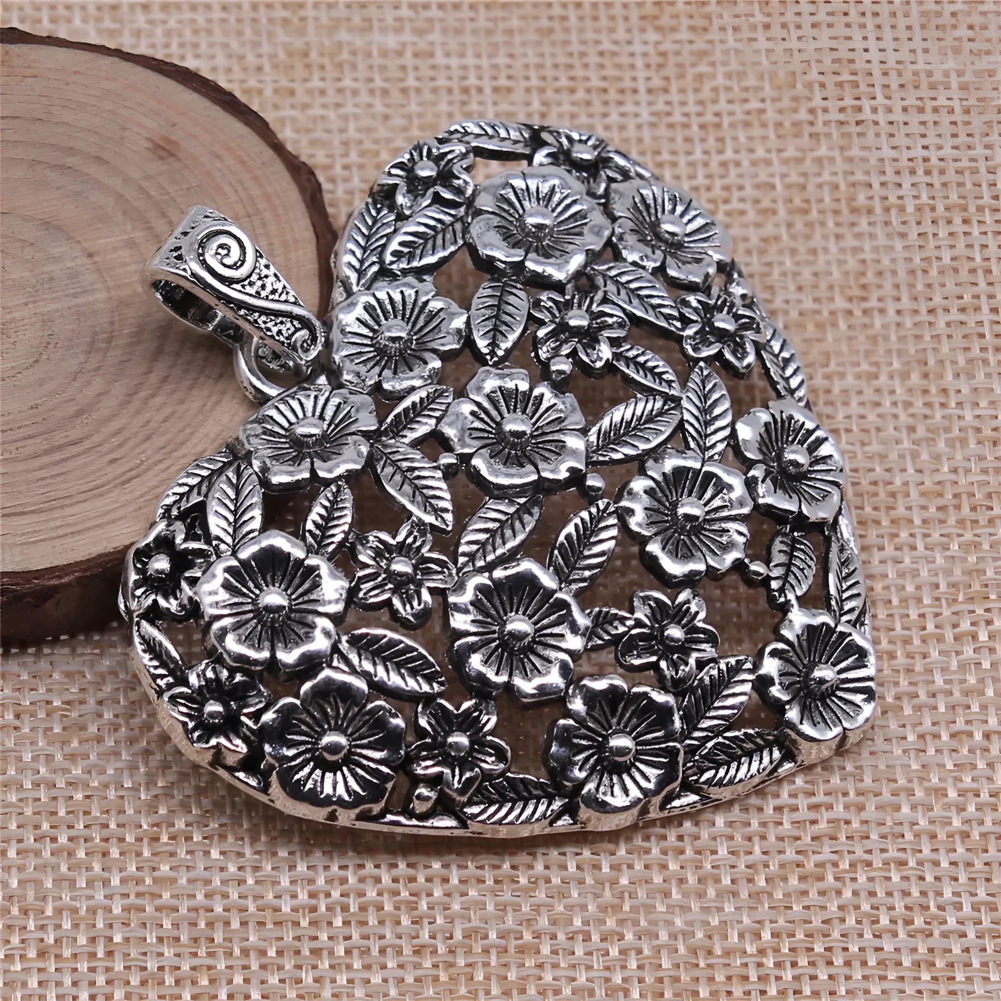 Close-up of a hollow flower love pendant in ancient silver colour, showing its detailed openwork design.