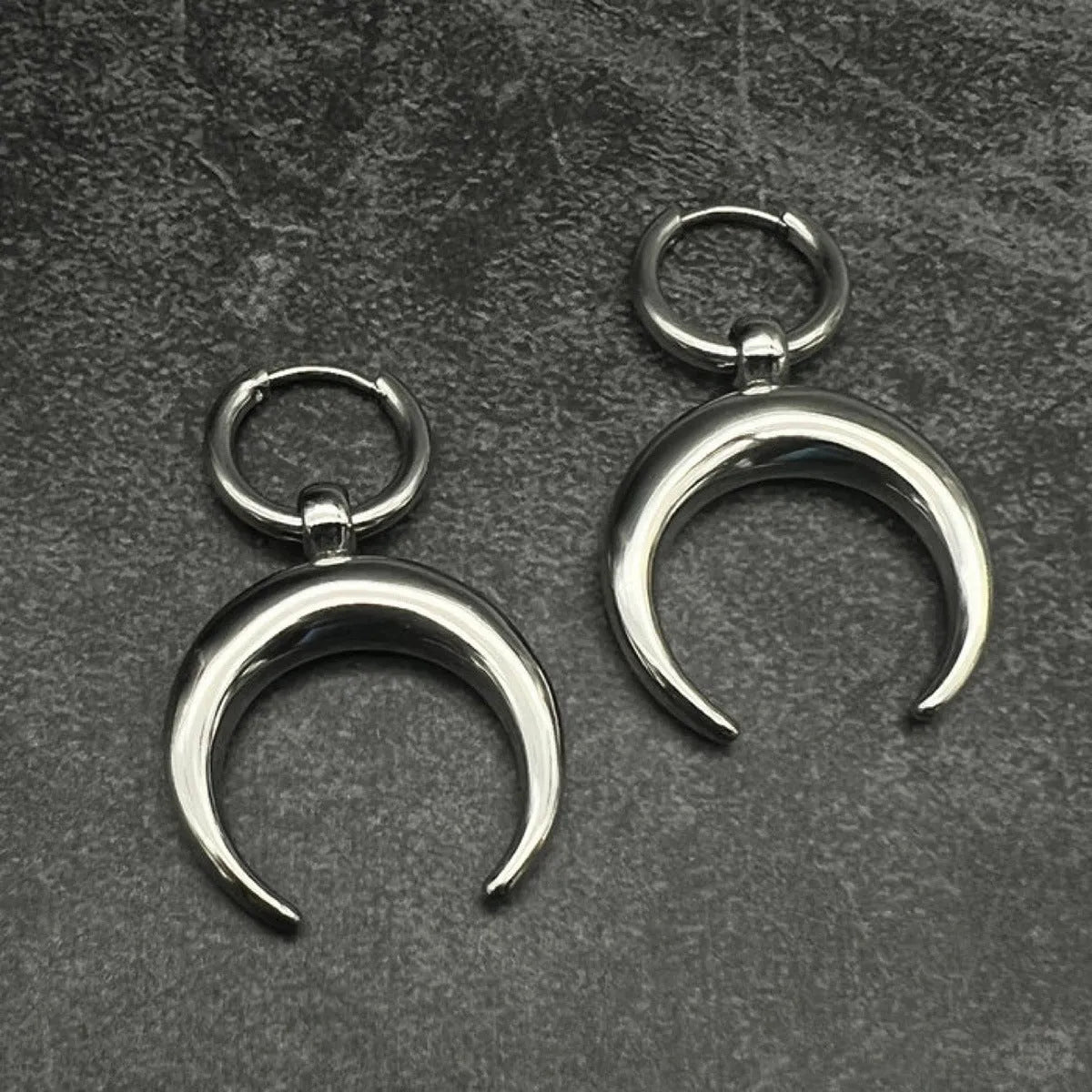 A pair of large silver geometric hoop earrings with a detailed Gothic moon motif, shown as clip-ons.