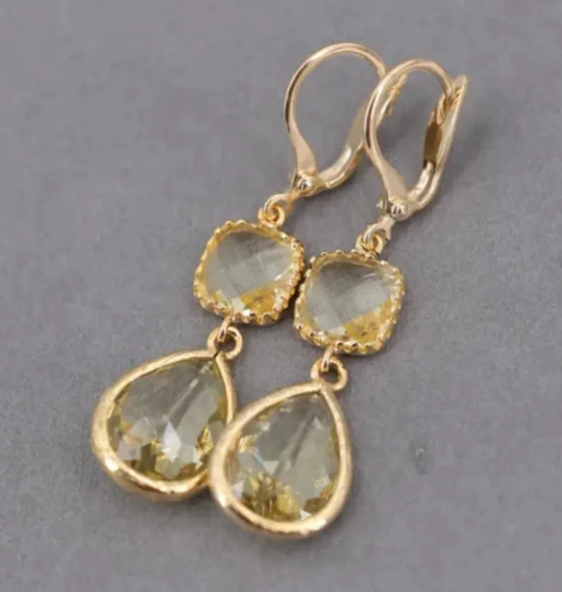 Gold geometric dangle earrings with a long fringe and water droplet design on a white background.