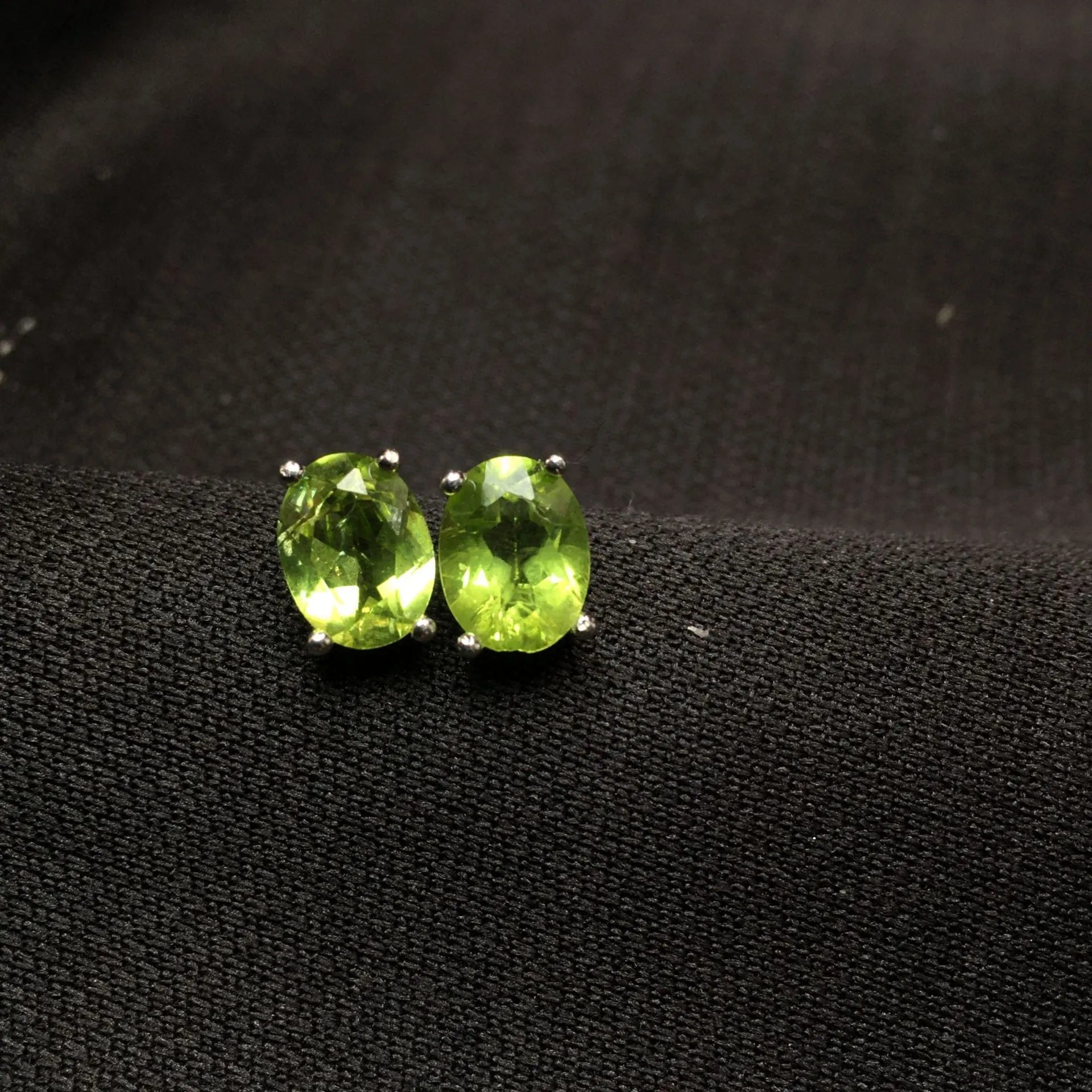 Close-up of grass green natural olivine stud earrings in S925 silver, showing ellipse-shaped stone.