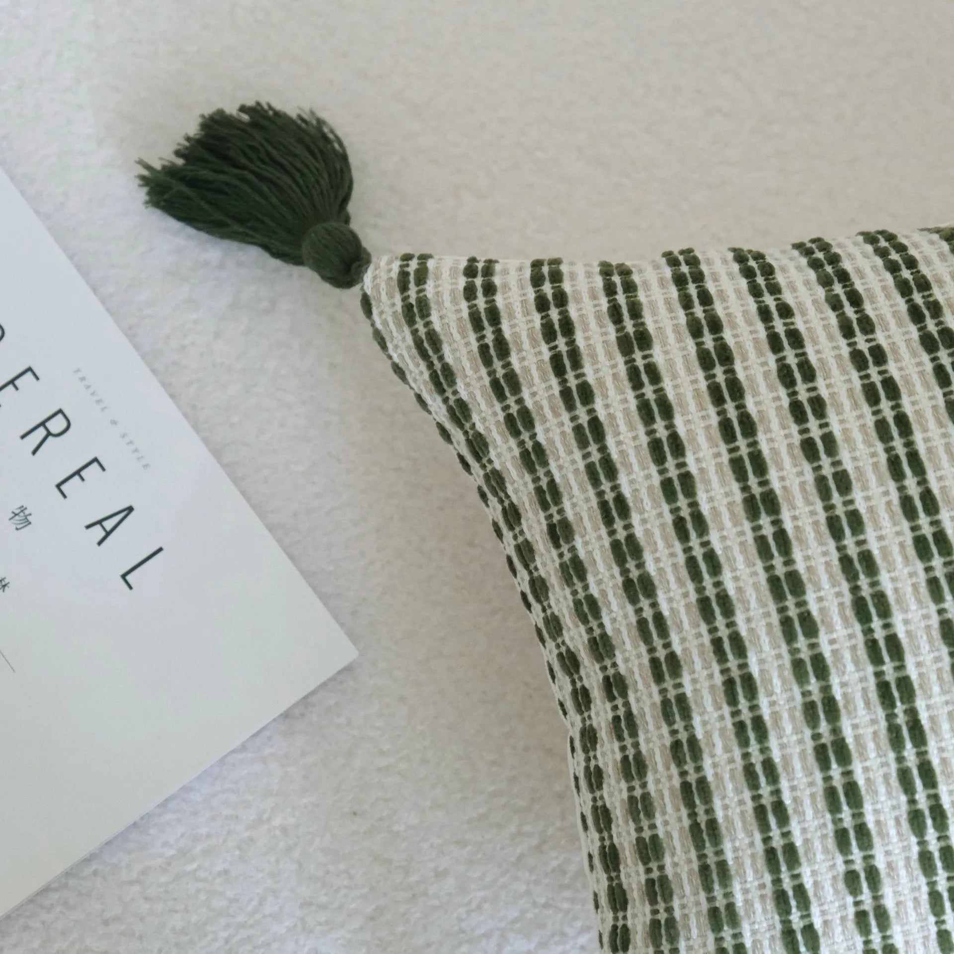 Green striped and botanical patterned hotel sample pillow with tassels on a bed display.
