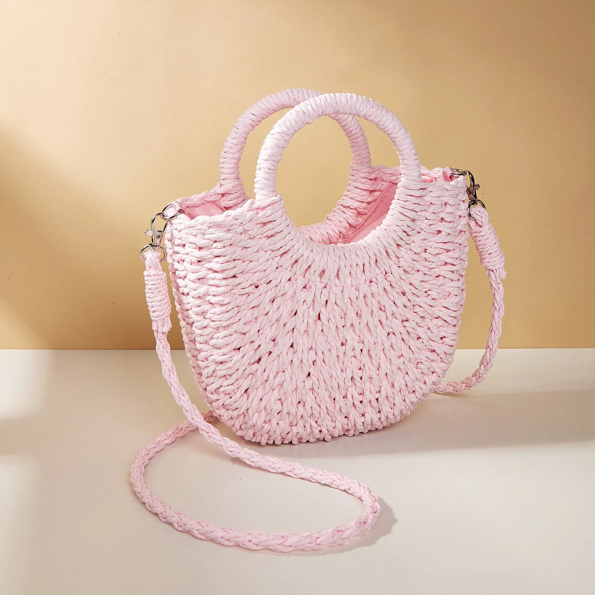 Woven straw beach bag in beige, peach skin lining, crossbody style, 24cm height, on a sandy beach