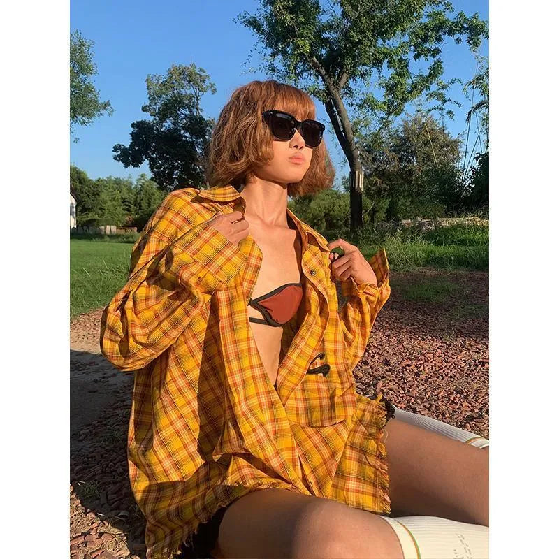 A loose yellow and black plaid shirt with a cardigan style, shown on a hanger.