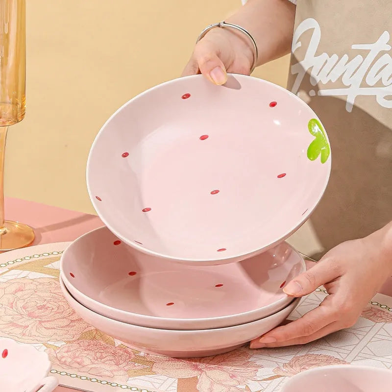 Cute strawberry pattern porcelain dinnerware set showing bowl, plate, and twist spoon on a table.