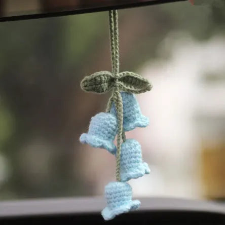 Green and white knitted wool car plant decoration with hanging rope on a car dashboard.