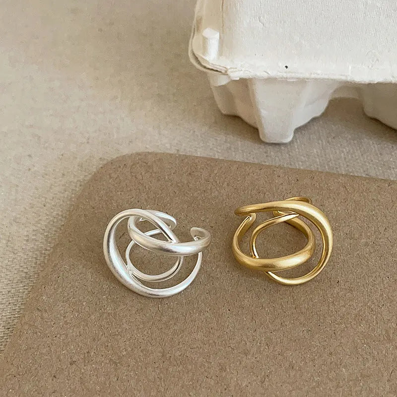 Geometric open ring with 3D interlaced matte metal design in gold or silver finish.