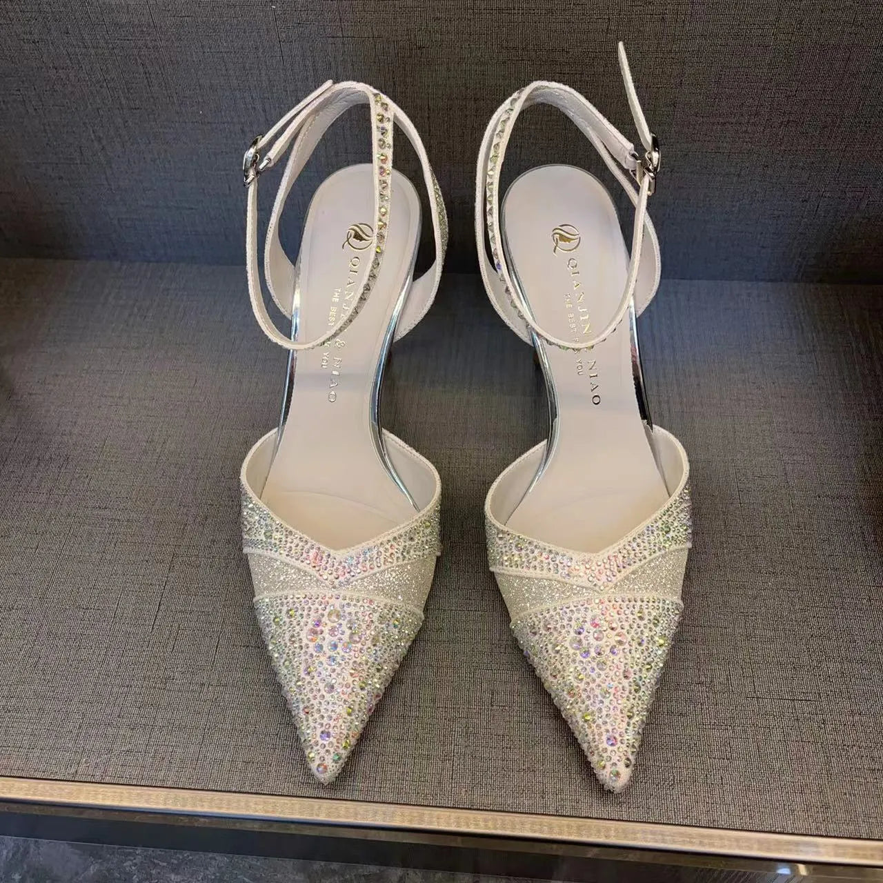 Women's silver high heel shoe with stiletto heel, pointed toe, and red sole on a white background.