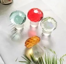 A set of colourful crystal mushroom decorations in transparent, green, red, and yellow on a white surface.