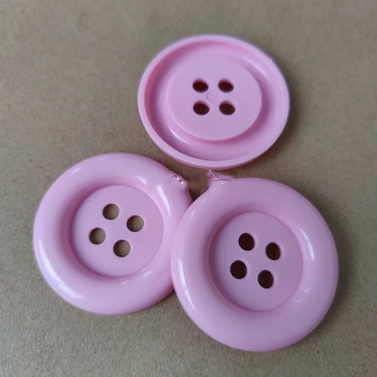 Assortment of oversized round plastic buttons in multiple colours with four stitching holes.