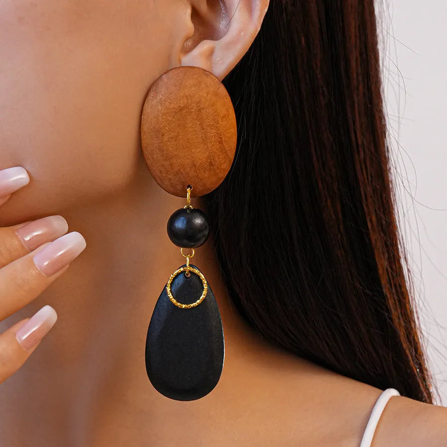 Close-up of handmade wooden elliptical earrings in silver, brown, and black colours on a retro-style background.