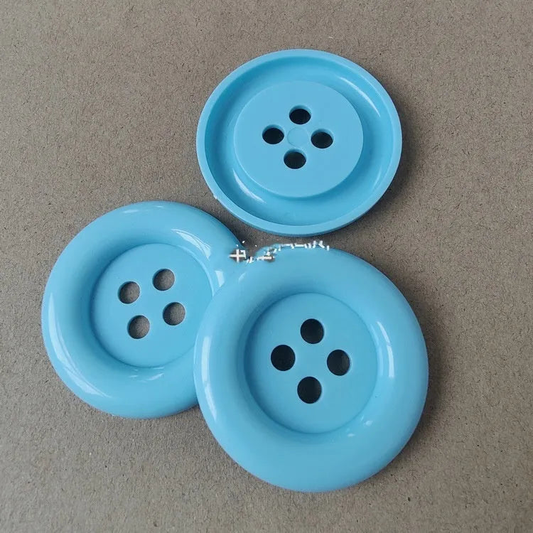 Assortment of oversized round plastic buttons in multiple colours with four stitching holes.