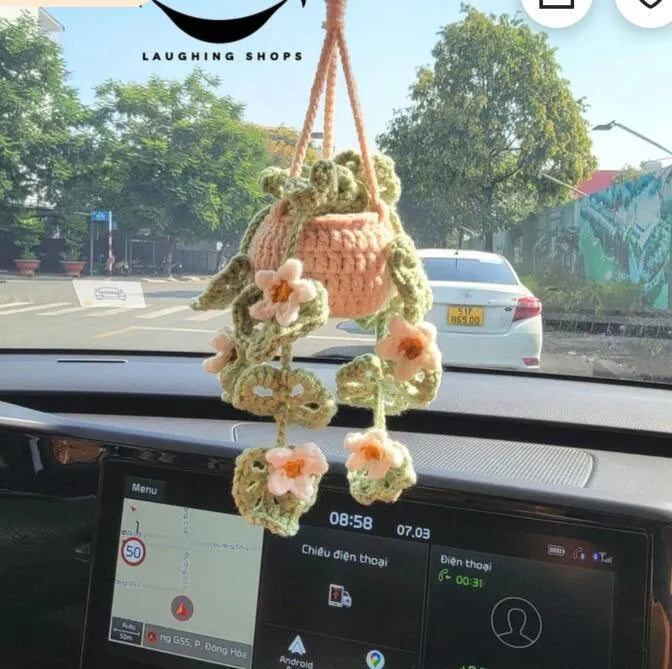 Green and white knitted wool car plant decoration with hanging rope on a car dashboard.