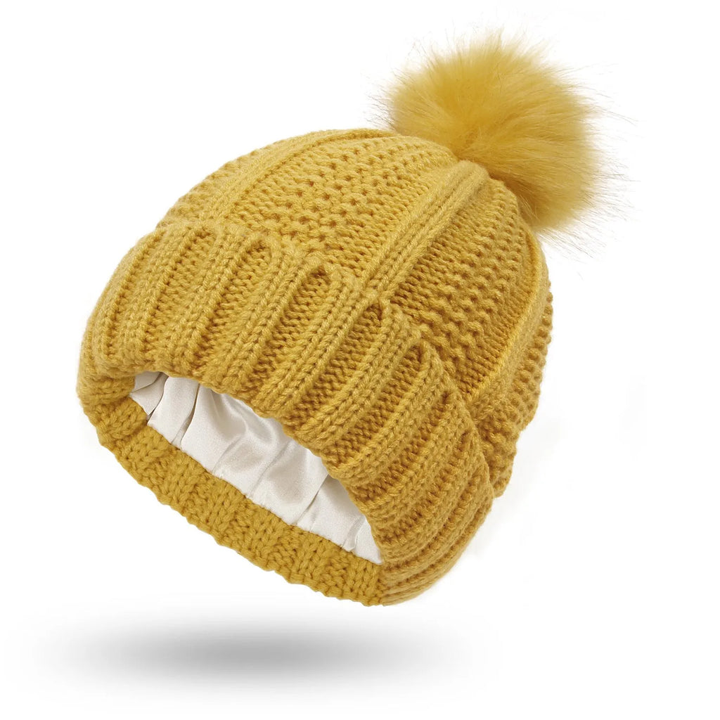 Women's knitted beanie hat with faux fur pom pom, shown in wine red, featuring a satin-lined interior.